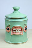Green ceramic jar with a face design on a white background